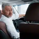 conception of success joyful bearded man in white shirt looks back while sitting in the modern car.jpg